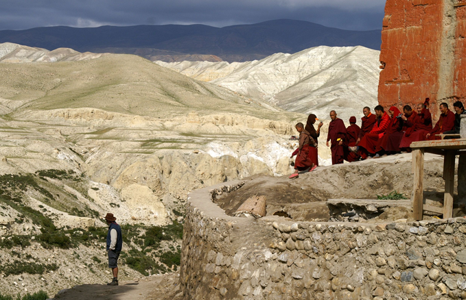 Lo Manthang, Upper Mustang, Nepal: An ATS traveller absorbs the scene and relaxed monks catch some late afternoon sun – looking across to Tibet where, unlike Mustang, the Buddhist monasteries have suffered decades of repression.
